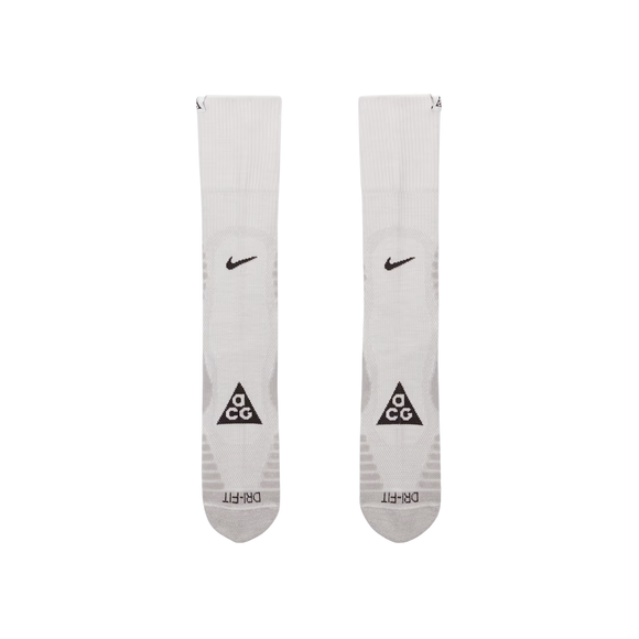 Nike ACG Crew Socks, Unisex i Summit White/Lt Smoke Grey, har sorte Swoosh-logoer i toppen og ACG-trekanter med DRI-FIT-tekst på foden, vist på en almindelig hvid baggrund. Fås i størrelserne S, M og L.