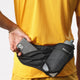 En person i en gul trøje lægger en smartphone ned i et sort Salomon Active Belt 3D Bottle, Unisex, hvor der også er plads til en letvægtsflaske.