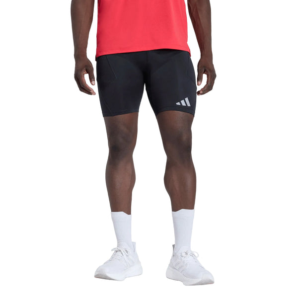 En person iført en rød trøje, sorte Adidas Adi365 Adaptive Running Half Tights til mænd, hvide strømper og hvide sneakers står foran en ensfarvet hvid baggrund. Ansigtet og overkroppen er ikke synlige.