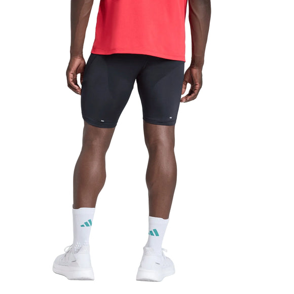 En person iført en rød trøje, Adidas Adi365 Adaptive Running Half Tights (Herre, sort), hvide sokker med et blåt logo og hvide sneakers står med ryggen til kameraet foran en ensfarvet hvid baggrund.