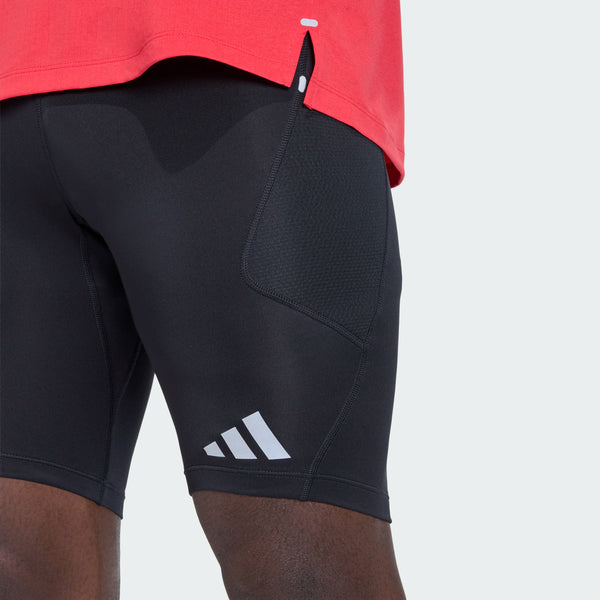 En person iført en rød trøje og sorte Adidas-træningsshorts med et hvidt logo i venstre søm, kombineret med Adi365 Adaptive Running Half Tights til mænd i sort fra Adidas, står foran en ensfarvet, lys baggrund.