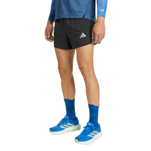 En person, der er klædt på til adidas-løbetræning, står foran en hvid baggrund iført en blå langærmet trøje, sorte Adidas Adi365 Climacool+ Pocket Shorts til mænd, blå sokker og blå Adidas-løbesko med hvide såler.