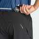 En person lægger en energigel-pakke i baglommen på et par sorte Adi365 Climacool+ Pocket Shorts, Herre fra Adidas, som har et Climalite-logo. Personen har en blå mønstret sportstrøje på, der er perfekt til adidas-løbetræning.