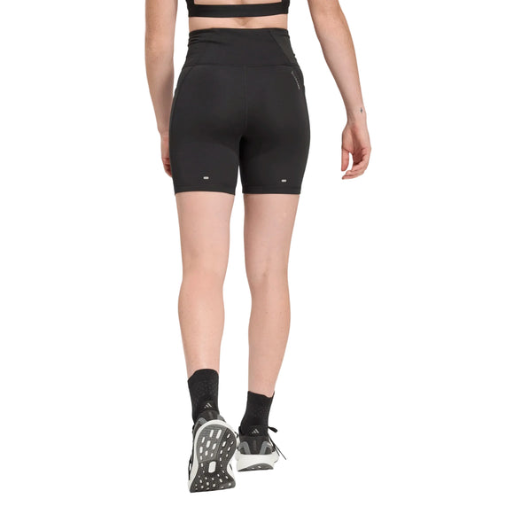 Der ses en person set bagfra, der går fremad foran en ensfarvet hvid baggrund. Personen har en sort Adidas-sport-bh på, sorte Adi365 Climacool Running Short Tights Dame fra Adidas, sorte strømper og sort-hvide sportssko.