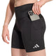En person iført sorte Adidas Adi365 Climacool løbetights til kvinder med en sidelomme lægger en smartphone i lommen. Disse shorts, der er inspireret af løbetights til kvinder og prydet med et lille hvidt Adidas-logo på venstre ben, forener stil og funktionalitet.