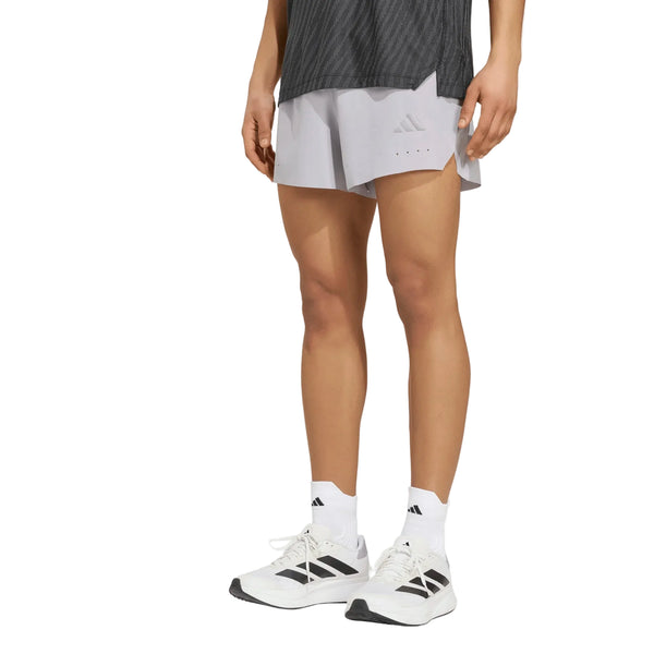 En person har Adidas Adi365 Climacool+ Pocket Shorts, Herre, Glogry, på, kombineret med en mørkegrå skjorte, hvide sokker med sorte Adidas-logoer og hvide Adidas-sneakers. Personen står foran en ensfarvet hvid baggrund; ansigtet kan ikke ses.