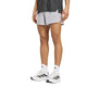 En person har Adidas Adi365 Climacool+ Pocket Shorts, Herre, Glogry, på, kombineret med en mørkegrå skjorte, hvide sokker med sorte Adidas-logoer og hvide Adidas-sneakers. Personen står foran en ensfarvet hvid baggrund; ansigtet kan ikke ses.