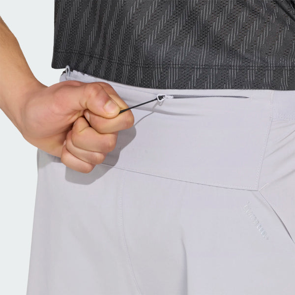 Et nærbillede bagfra af en person, der justerer snoren i taljen på et par Adidas Adi365 Climacool+ Pocket Shorts, Herre, Glogry. Personen har en mørk, struktureret skjorte på.
