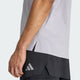 En person iført en lysegrå Adidas Adi365 Running Aspyre T-shirt (Herre, Glogry) med små huller og sorte shorts med et gråt Adidas-logo. Billedet viser venstre side af vedkommendes overkrop og arm.