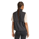 På billedet ses en person set bagfra med langt, flettet hår, iført en beige kortærmet bluse, sorte leggings og Adidas Adi365 Running Essentials-vest til kvinder i sort på en ensfarvet hvid baggrund.