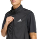 Herre har en sort Adi365 Running Essentials-vest fra Adidas på – en kortærmet sportsvest, der er delvist åbnet, så det karakteristiske hvide adidas-logo på brystet fremstår tydeligt mod en ensfarvet lys baggrund.