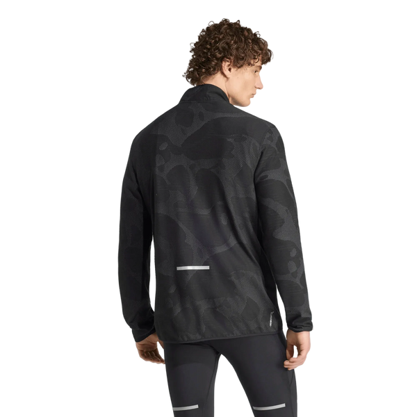 Der ses et billede bagfra af en person med krøllet hår, der bærer Adidas Adi365 Running Half Zip langærmet trøje til mænd i farven Black/Grefiv, som har et diskret camouflagemønster og reflekterende detaljer, kombineret med sorte træningsbukser. Adi365 Running Half Zip-trøjen skiller sig tydeligt ud mod den ensfarvede hvide baggrund.