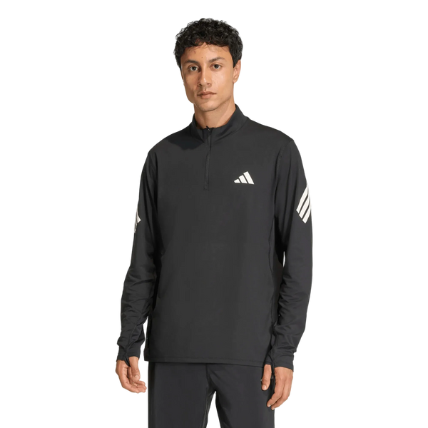 En person står med ansigtet fremad og har den sorte Adi365 Running Iconc Half Zip herre-trøje fra Adidas på. Denne langærmede trøje har en kvart lynlås og er prydet med hvide Adidas-logoer på brystet og ærmerne. Den ensfarvede hvide baggrund fremhæver denne stilfulde løbetrøje til mænd.