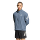 En person med flettet hår har en blå Adidas Adi365 Running Iconic-jakke, Herre, Onix/Refsil, med hvide striber på ærmerne og sorte shorts med hvide striber på, og står foran en ensfarvet hvid baggrund.
