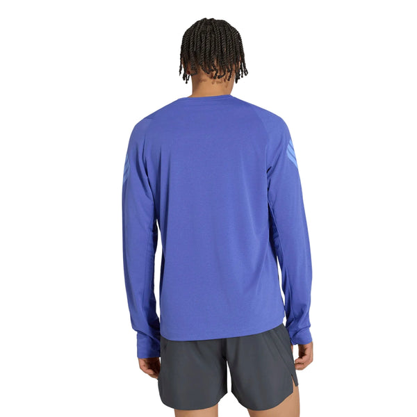 En person set bagfra, iført en blå Adidas Adi365 Running Iconic langærmet trøje og mørke sportsshorts.