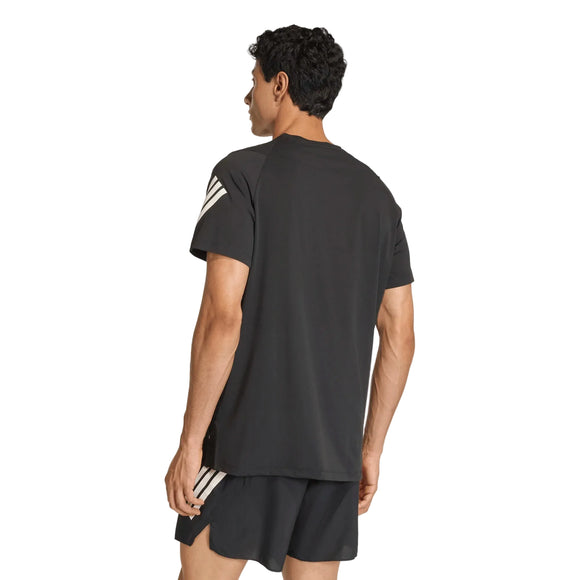 En person står med ryggen til kameraet iført en Adidas Adi365 Running Iconic T-shirt, Herre, sort med hvide striber på ærmerne og sorte shorts. Climacool-stoffet i denne Adidas-T-shirt sikrer en kølig og behagelig fornemmelse på den ensfarvede hvide baggrund.