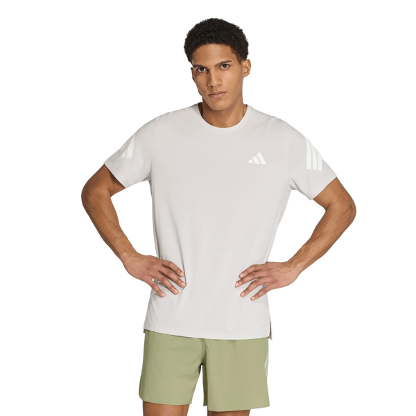 En person står med hænderne i siden og har en Adidas Adi365 Running Iconic T-shirt til mænd i farven Greone/White på, der er prydet med Adidas-logoet og de karakteristiske hvide striber på ærmerne, kombineret med lysegrønne shorts. Baggrunden er ensfarvet hvid.