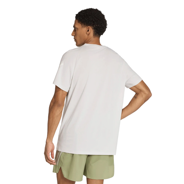En person står med ryggen til og har en Adidas Adi365 Running Iconic T-shirt til mænd i farven Greone/White på samt lysegrønne shorts. Baggrunden er ensfarvet hvid, og personens venstre arm er bøjet, mens hånden hviler på hoften.
