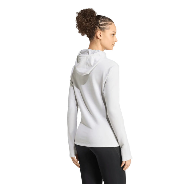 En person med krøllet hår sat i cornrows, der står med ryggen til kameraet foran en ensfarvet hvid baggrund, har en Adidas Adi365 Running Winterized langærmet trøje i farven Greone på.