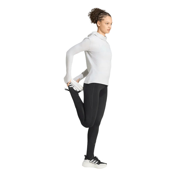 En person iført en hvid Adi365 Running Winterized langærmet trøje fra Adidas, sorte leggings og sorte Adidas-sneakers står på det ene ben og holder den anden fod bag sig i en stående lårstrækning foran en hvid baggrund.