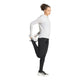 En person iført en hvid Adi365 Running Winterized langærmet trøje fra Adidas, sorte leggings og sorte Adidas-sneakers står på det ene ben og holder den anden fod bag sig i en stående lårstrækning foran en hvid baggrund.