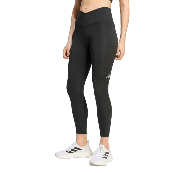 En kvinde har Adidas Adi365 Seasonal 7/8-tights til kvinder i sort på – tights med høj talje og et lille logo på venstre lår – kombineret med hvide sportssko, mens hun står foran en ensfarvet hvid baggrund.