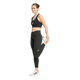 En kvinde iført sorte Adidas Adi365 Seasonal 7/8-tights står på det ene ben og holder den anden fod bag sig for at strække låret. Hun har hvide sneakers på og ser fremad med et neutralt udtryk foran en ensfarvet hvid baggrund.