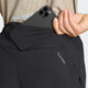 En kvinde putter en sort smartphone ned i den bageste lynlåslomme på et par sorte Adi365 Climacool+2 Pocket Shorts 5" fra Adidas, og et nærbillede viser AEROREADY-logoet på disse hurtigtørrende shorts.
