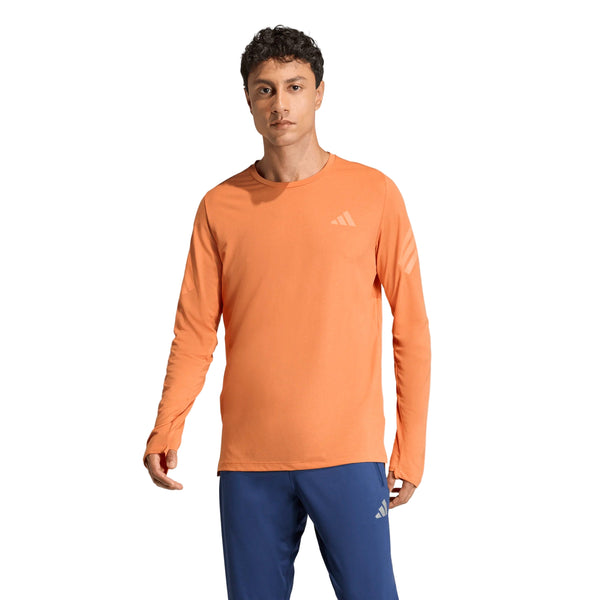 En mand iført en orange Adidas Adi365 Longsleeve Shirt (Herre) og blå bukser står med front mod en almindelig hvid baggrund.