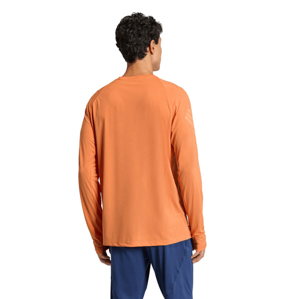 En person med kort, krøllet mørkt hår ses bagfra iført en orange Adidas Adi365 Longsleeve Shirt for men og blå bukser på en almindelig hvid baggrund.