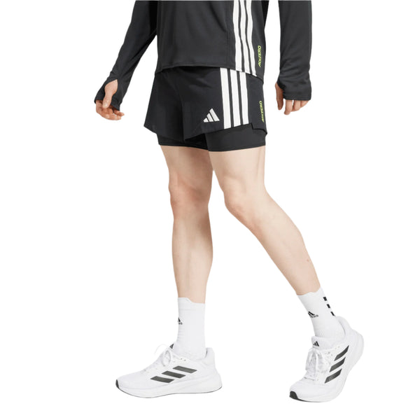 En person iført en sort langærmet top, Adidas Adizero Running 2-IN-1 Gel Pocket Shorts til mænd i sort, hvide Adidas-sokker og hvide Adidas-sneakers går mod en hvid baggrund.