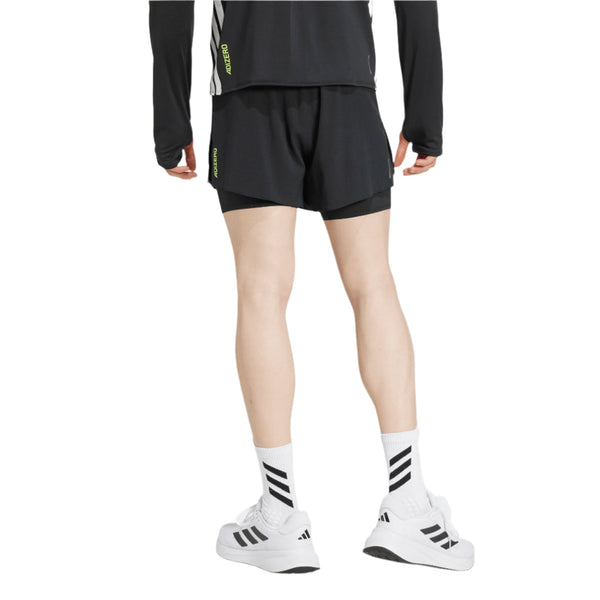 En person vender ansigtet væk fra kameraet og er iført en sort langærmet trøje, Adidas Adizero Running 2-IN-1 Gel Pocket Shorts i sort, hvide strømper med sorte striber og hvide adidas-sneakers med sorte logoer på både strømper og sko.