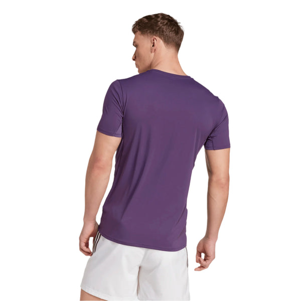 En person, der vender væk fra kameraet, er iført en lilla Adidas Adizero E Tee, Herre, Aurplu t-shirt og hvide shorts og står på en hvid baggrund.