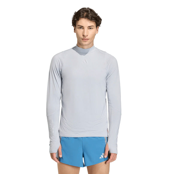 En person står med ansigtet fremad og er iført en lysegrå Adidas Adizero Hakone Ekiden Longsleeve, Herre, Halsil og blå sportsshorts på en almindelig hvid baggrund.