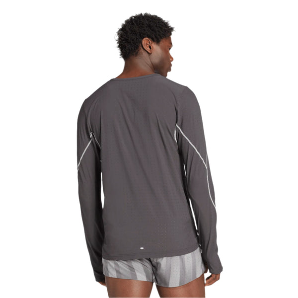 En person med kort krøllet hår står med ryggen til kameraet iført en sort Adidas Adizero P Ls M langærmet T-shirt til mænd lavet af genbrugsmateriale og lysegrå og hvidstribede shorts.