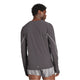 En person med kort krøllet hår står med ryggen til kameraet iført en sort Adidas Adizero P Ls M langærmet T-shirt til mænd lavet af genbrugsmateriale og lysegrå og hvidstribede shorts.