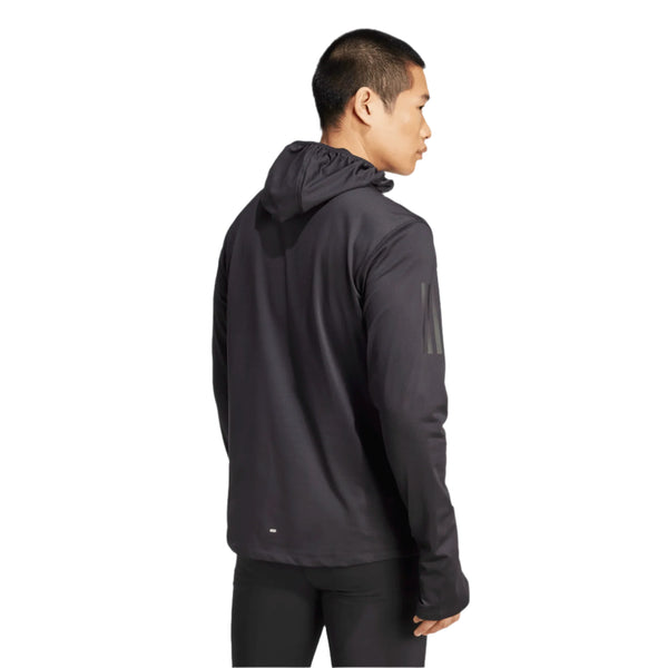 En mand med kort sort hår er iført Adidas Otr Bin Hz herre løbejakke i sort med CLIMAWARM-teknologi og sorte bukser, mens han står på en hvid baggrund og kigger væk fra kameraet.