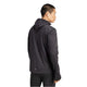 En mand med kort sort hår er iført Adidas Otr Bin Hz herre løbejakke i sort med CLIMAWARM-teknologi og sorte bukser, mens han står på en hvid baggrund og kigger væk fra kameraet.