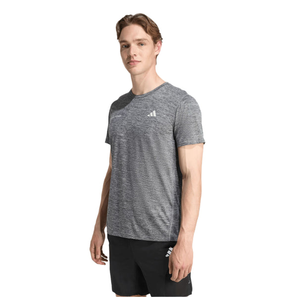 En mand står og kigger lidt til siden iført en Adidas Otr Mel Tee M til mænd i sort/grød og sorte shorts med hvide Adidas-logoer på en almindelig hvid baggrund.