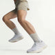 En kvinde midt i et spring, vist fra benene og ned, er iført beige sportsshorts og Adidas Adizero Evo SL Dame Ftwwht/Ftwwht/Warsan-sneakers med lysegrå strømper på en almindelig hvid baggrund.
