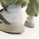 Nærbillede af en person iført Adidas Adizero Evo SL, Herre i Owhite/Aucome/Msilve med hvide sokker og grønne bukser, der er stoppet ned. Fokus på hælen og Adidas-branding, der fremhæver LIGHTSTRIKE PRO-dæmpningen.