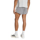 En person står med ryggen til kameraet og er iført en lysegrå skjorte, Adidas Adizero Archive 5″ løbeshorts til mænd i farven Grethr/Greone, hvide strømper og hvide sportssko med sorte striber. Baggrunden er helt hvid.