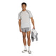 En mand er iført en adidas Adizero Archive løbetrøje til mænd i farven Greone/Grethr, matchende grå shorts, hvide og grå Adidas-sneakers, hvide sokker og holder en grå jakke i hånden. Baggrunden er ensfarvet hvid.