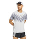 En mand står med hænderne bag ryggen og har en hvid og grå Adidas Adizero Aspyre Running Climacool-T-shirt på, sorte Adidas-shorts med hvide striber og en hvid og sort Adidas-kasket. Han kigger til venstre.