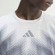 Nærbillede af en person, der bærer en hvid Adidas Adizero Aspyre Running Climacool-T-shirt med et gråt Adidas-logo og et abstrakt stribemønster, der fremhæver T-shirtens slanke design. Kun den nederste del af ansigtet, halsen og den øverste del af brystet er synlige på en ensfarvet, lys baggrund.