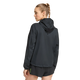 En kvinde med lysebrunt, flettet hår er iført en sort Adidas Adizero Running Blaze-jakke og sorte shorts. Hun står med ryggen til kameraet og hovedet vendt til siden foran en ensfarvet hvid baggrund.