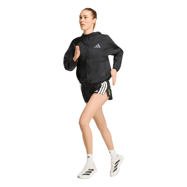 En person iført en sort Adidas Adizero Running Blaze-jakke og sorte shorts med hvide striber løber i hvide sokker og hvide sko med sorte detaljer foran en ensfarvet hvid baggrund.