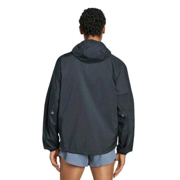 En person står med ryggen til kameraet iført en Adidas Adizero Running Blaze-jakke, herre, sort, kombineret med lyseblå shorts foran en ensfarvet hvid baggrund.