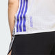 En person har en Adidas Adizero løbetrøje på, Dame, hvid/Solpur med lilla striber og »ADIZERO« på siden, kombineret med sorte shorts med en hvid stribe. Kun overkroppen og de øverste dele af benene er synlige.