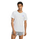 En mand med kort, krøllet hår har en Adidas Adizero løbetrøje (herre) i farven White/Solpur på og grå shorts. Løbetrøjen har et lille logo på brystet, mens han står med ansigtet fremad, den ene arm afslappet og den anden let bøjet.